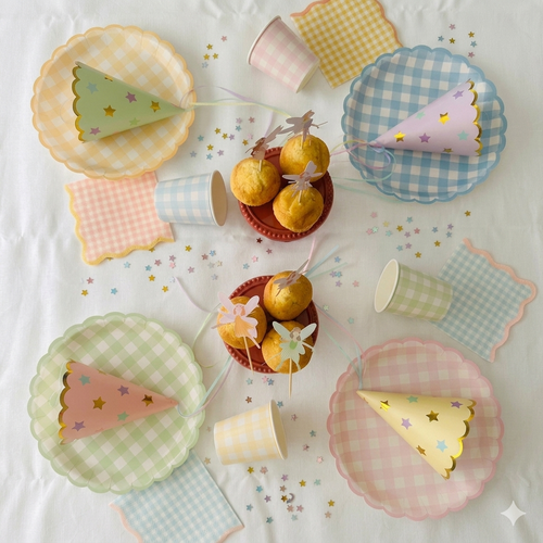 Set completo de decoración para fiesta de hadas y princesas con platos de cuadros vichy pastel, vasos, servilletas, gorritos de fiesta y confeti de estrellas sobre un mantel blanco.
