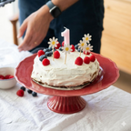 Tarta de primer cumpleaños decorada con toppers de margaritas y vela rosa, parte de la colección de fiesta premium El Jardín de las Margaritas.