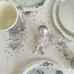 Detalle de mesa dulce con magdalenas decoradas con toppers de cohetes y astronautas sobre un plato plateado, rodeado de menaje de fiesta espacial.