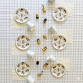 Flat lay product photography of a full kids birthday table setting featuring construction truck paper plates, blue checkered cups, and toy excavators on a black and white grid paper tablecloth.